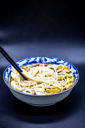 Udon noodles with vegetables and chopsticks on a black background