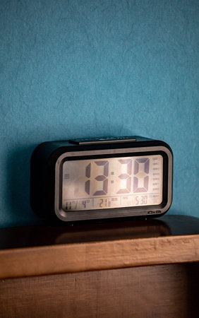 Digital alarm clock on a wooden shelf against a blue wall background.
