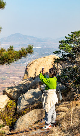 Young woman tourist taking photo with mobile phone on the top of a mountainの写真素材