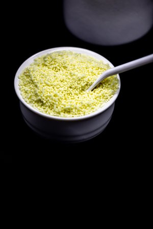 Raw couscous in a bowl on a black background. Selective focus.