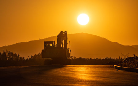 Silhouette of a bulldozer working on a road at sunsetの写真素材