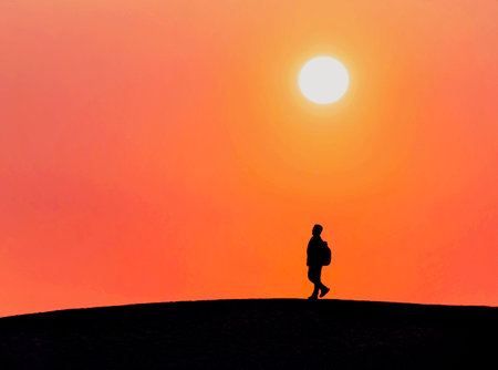 Silhouette of a man walking on top of sand dune at sunsetの写真素材