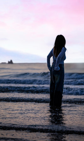 Silhouette of a young woman standing on the beach at sunsetの写真素材