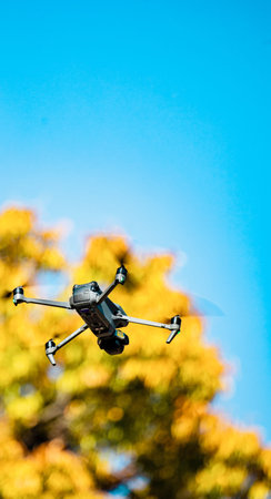 Drone flying in the blue sky with autumn leaves in the background