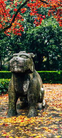 Stone lion statue in the park with autumn leaves falling on ground.の写真素材