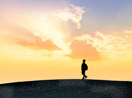 Silhouette of a man walking on sand dune at sunsetの写真素材