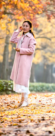 Young woman in pink coat walking in autumn park with yellow leaves.のeditorial素材