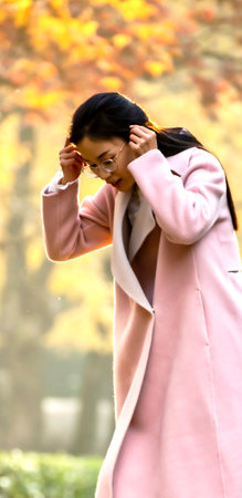 Asian woman in pink coat and eyeglasses in autumn park.のeditorial素材
