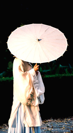 Asian woman in traditional costume with white umbrella in the park at nightの写真素材