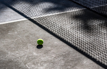 Tennis ball on tennis court with shadow of net on the floorの写真素材
