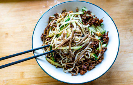 Chinese noodles with beef and vegetables in a bowl on a wooden tableの写真素材