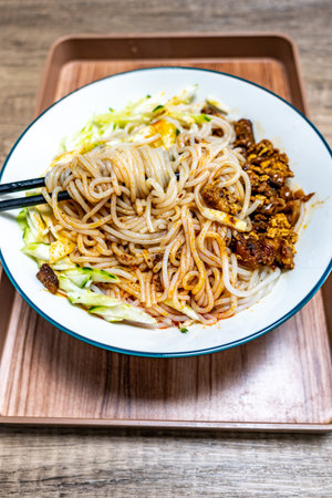 Noodles with minced pork and vegetables in white bowl on wooden tableの写真素材
