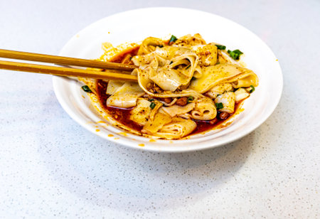 Rice noodles with squid in spicy sauce with chopsticks on white plateの写真素材