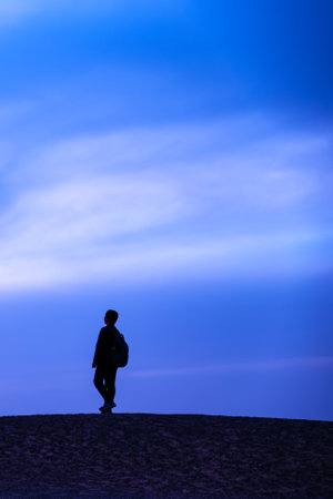 Silhouette of a man walking on sand dune at sunsetの写真素材