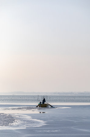 Fisherman in a boat on the ice of a frozen lakeの写真素材