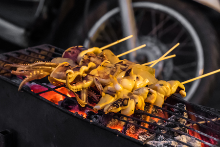 Squids on spit being grilled over red glowing coalの写真素材
