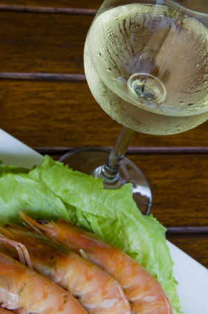 Fresh king prawns placed on a bed of lettuce served with a pink sauce and slices of lemons accompanied by a glass of white wine in an outdoor setting.の写真素材