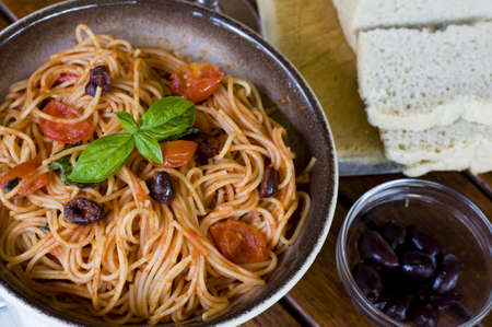A plate of spaghetti with italian sauce, served with red wine, bread and olives on a wooden tableの写真素材