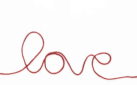A string of red wool forms the word love on a white backgroundの写真素材