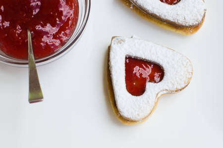 Heart shape strawberry jam cookies placed on a white plate with jam and red backgroundの写真素材