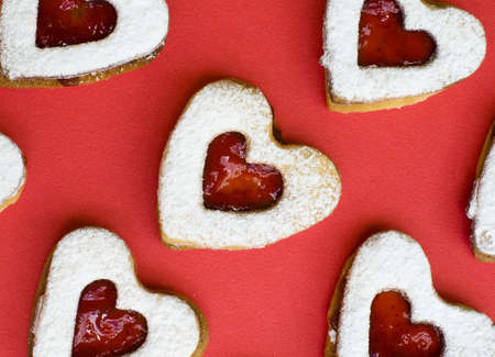 Heart shape strawberry jam cookies placed on a white plate with jam and red backgroundの写真素材