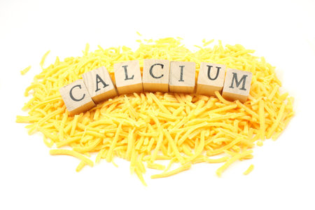 Mound of shredded cheddar cheese with the word calcium on wooden blocks placed in the middle of ound on white backgroundの写真素材