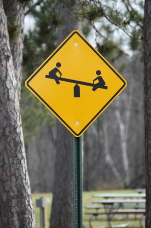 Photograph of a children at play sign with a teeter totter on it as a sign notifying drivers that a playground is aheadの写真素材