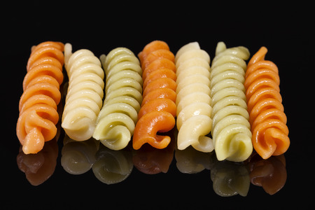 Colored spiral pasta isolated on black background, reflectionの写真素材