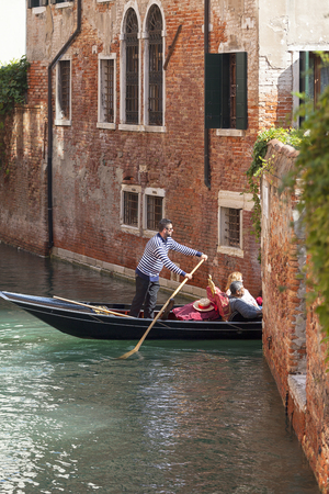 VENICE, ITALY-SEPTEMBER 22, 2017: Venetian gondolier rowing through the narrow canal. Gondola is iconic traditional boat, very popular means of transport for touristsのeditorial素材