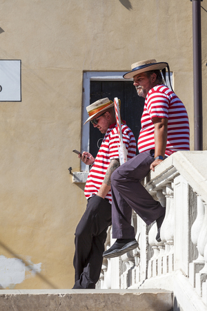 VENICE, ITALY - SEPTEMBER 22, 2017 :Two gondoliers in traditional costumes on the bridge during a rest break. Gondola is iconic traditional boat, very popular means of transport for touristsのeditorial素材