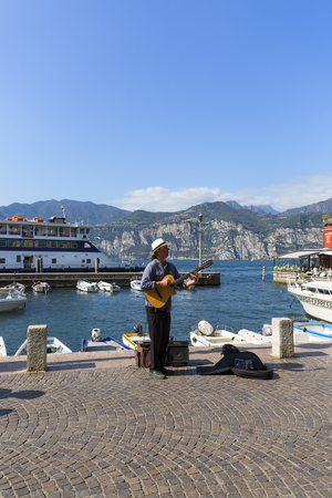 MALCESINE, ITALY - SEPTEMBER 30, 2018 : Lake Garda, the largest lake in Italy, port for boats, man playing the guitar on the coastのeditorial素材