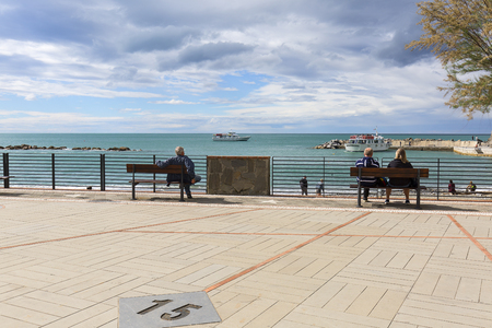 MONTEROSSO, CINQUE TERRE - ITALY, MAY 12, 2019: View on sea from the waterfront, people sitting on benches looking at the water, Ligurian Rivieraのeditorial素材