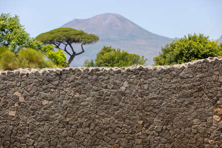 A fragment of the ancient wall in city destroyed by the eruption of the volcano Vesuvius in 79 AD near Naples. In the background mountain Vesuvius volcano, Pompeii, Italyの写真素材