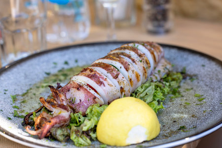 Traditional greek cuisine, grilled squid with piece of lemon and green salad, dish on a plate in a...