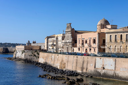 Syracuse, Sicily, Italy - April 29, 2023: Beautiful view of promenade Lungomare d'Ortygia by Ionian Sea. Facade of Church of the Holy Spirit and picturesque Cala Rossa Beachのeditorial素材