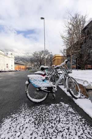 Innsbruck, Austria - February 26, 2023: Snow-covered bicycles parked in Rennplatz square in front of Hofburg, former Habsburg palace. Peaks of the snowy Alps mountains in the clouds in the distanceのeditorial素材