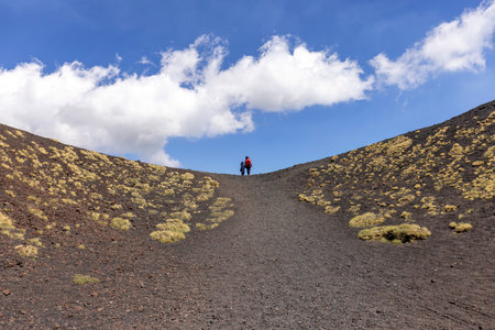 Mount Etna, Sicily, Italy - April 27, 2023: Two people walking the path of the slopes of the volcano Mount Etna on the sunny day. Stones and solidified lava, withered vegetationのeditorial素材