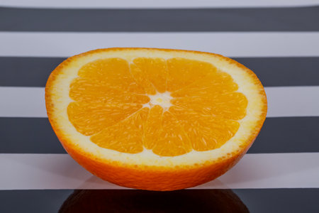 Half a fresh orange lying on a black and white striped tablecloth, close upの写真素材