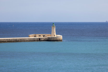 Valletta, Malta - April 17, 2025: Lighthouse and St. Elmo Breakwater, leading from Fort Saint Elmo through Grand Harbour, surrounded by calm blue water of Mediterranean Seaの写真素材
