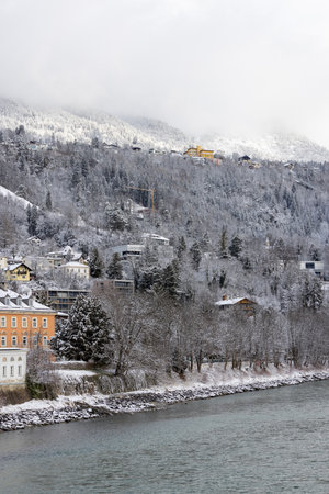 View of slope of Alps over the Inn River with typical buildings on a cloudy winter day in the city center, Innsbruck; Tyrol, Austriaの写真素材
