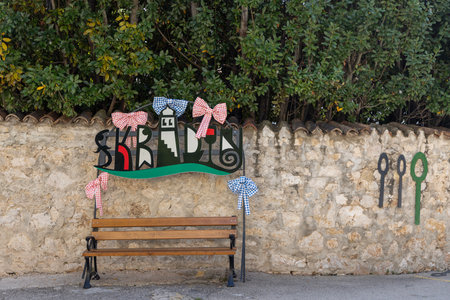 Skradin, Croatia - September 16, 2025: Colorful Skradin sign with decorative bows above a wooden bench against a stone wall. City is located near Krka National Parkのeditorial素材