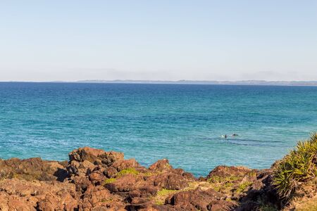 Sunny morning, two surfers waiting for waves with jagged rocks in the foreground. Copy spaceの写真素材