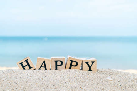 Wooden dice with letters HAPPY placed on the sand on the beachの写真素材