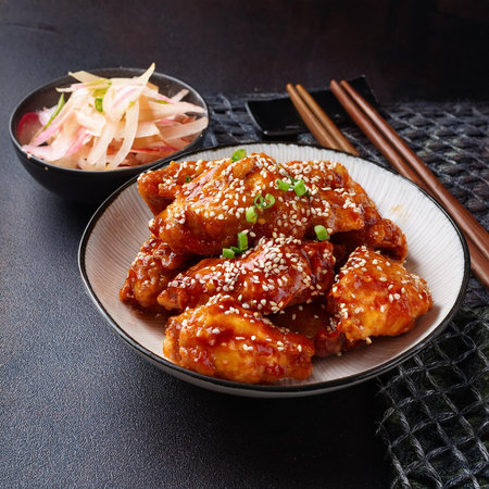 Baked chicken wings with sesame seeds in bowl on black backgroundの素材