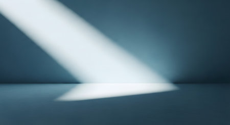 An empty, moody room with a textured blue-grey wall and floor, illuminated by a single, dramatic diagonal beam of bright white light.の素材