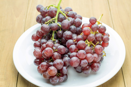 red bunch grape in white dish on wooden boardの写真素材