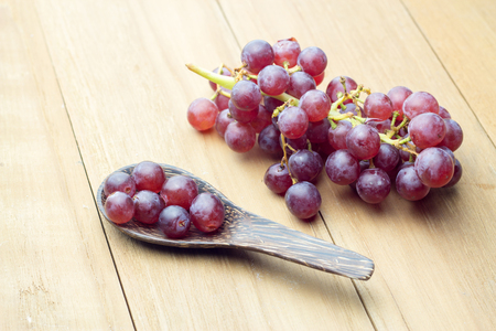grape in wood spoon and bunch grape on wooden board still lifeの写真素材