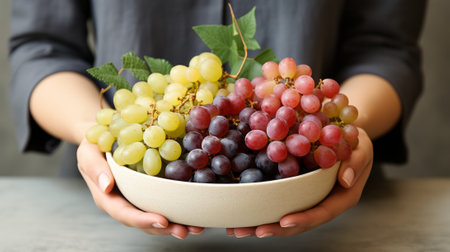 A person holds a bowl of vitis grapes, their fingers delicately grasping the succulent fruit, embodying the essence of nourishment and vitality in this indoor scene of produce perfectionの素材