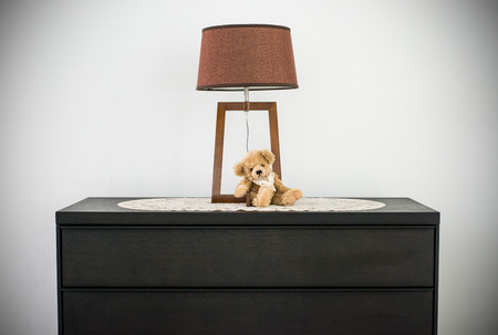 Teddy bear sitting next the urban classic lamp on the black wooden cabinetの写真素材