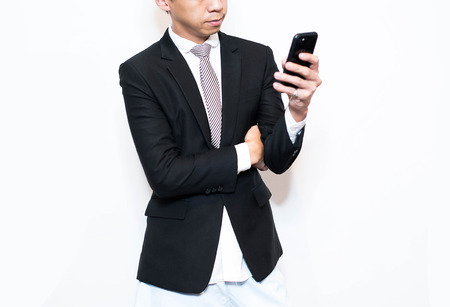 Young business man looking reading his phone about work and thinking as a business concept isolated on white backgroundの写真素材
